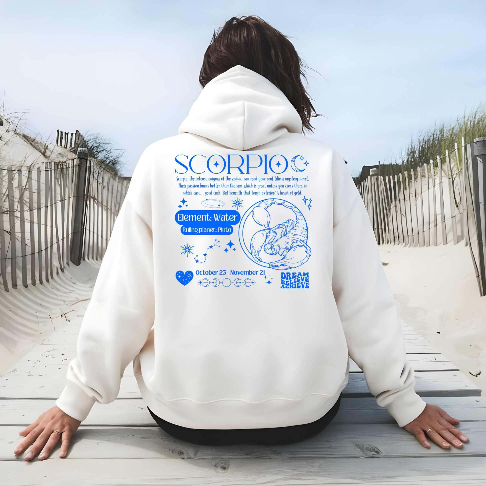 White Scorpio-themed hoodie with a blue zodiac design on the back, featuring the Scorpio symbol, element Water, ruling planet Pluto, and a message about Scorpio's intense personality traits. Includes dates, moon phases, and inspirational words 'Dream, Believe, Achieve