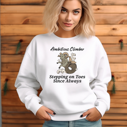 Front of white Capricorn-themed sweatshirt with a playful design featuring a Capricorn goat character and the text 'Ambitious Climber - Stepping on Toes Since Always.