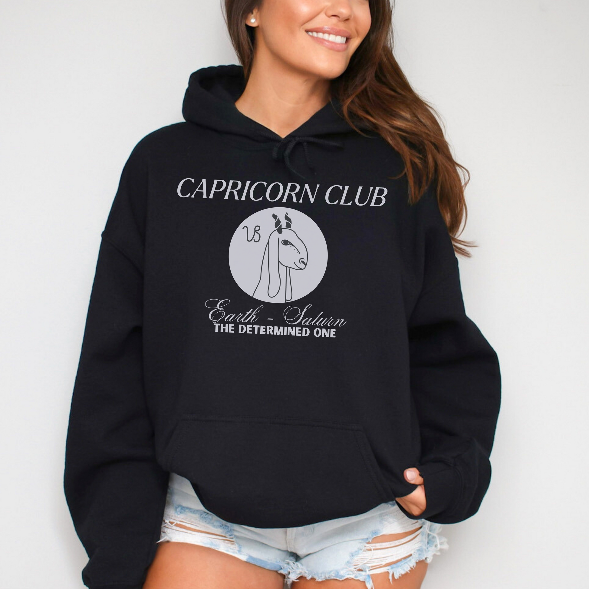 Front of black Capricorn-themed hoodie with 'Capricorn Club' text, Capricorn symbol illustration, and phrase 'Earth - Saturn, The Determined One.