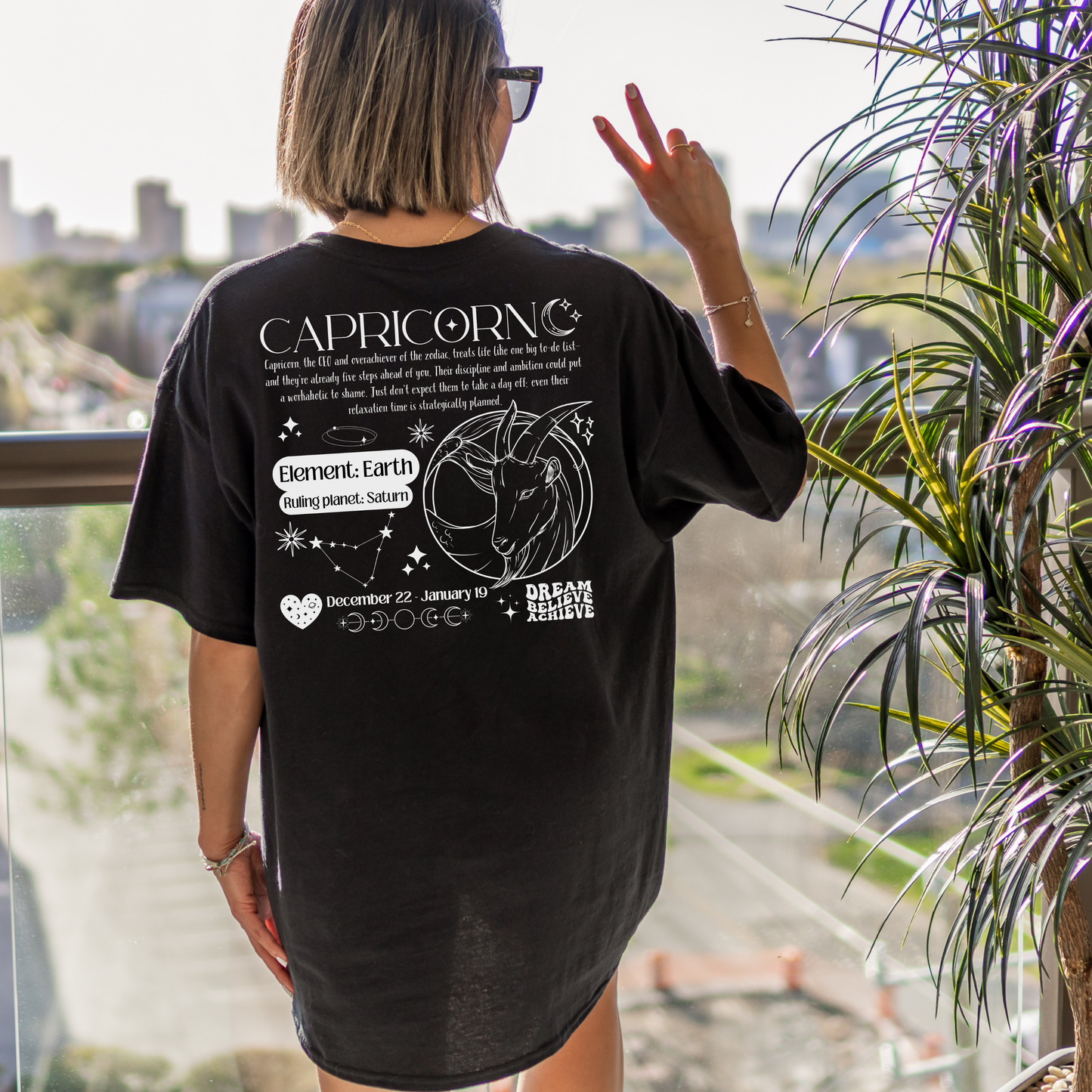 Back of black Capricorn-themed t-shirt with retro design, featuring Capricorn text, symbol, element 'Earth,' ruling planet 'Saturn,' date range December 22 - January 19, and motivational phrases 'Dream, Believe, Achieve.