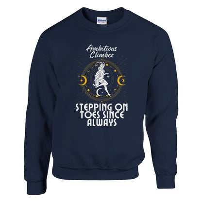 Front of navy blue Capricorn-themed sweatshirt with retro design, featuring text 'Ambitious Climber' above an illustration of a determined figure, surrounded by celestial symbols, and 'Stepping on Toes Since Always' below.