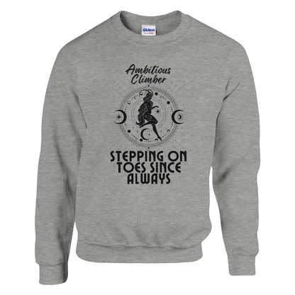 Front of sport grey Capricorn-themed sweatshirt with retro design, featuring text 'Ambitious Climber' above an illustration of a determined figure, surrounded by celestial symbols, and 'Stepping on Toes Since Always' below.