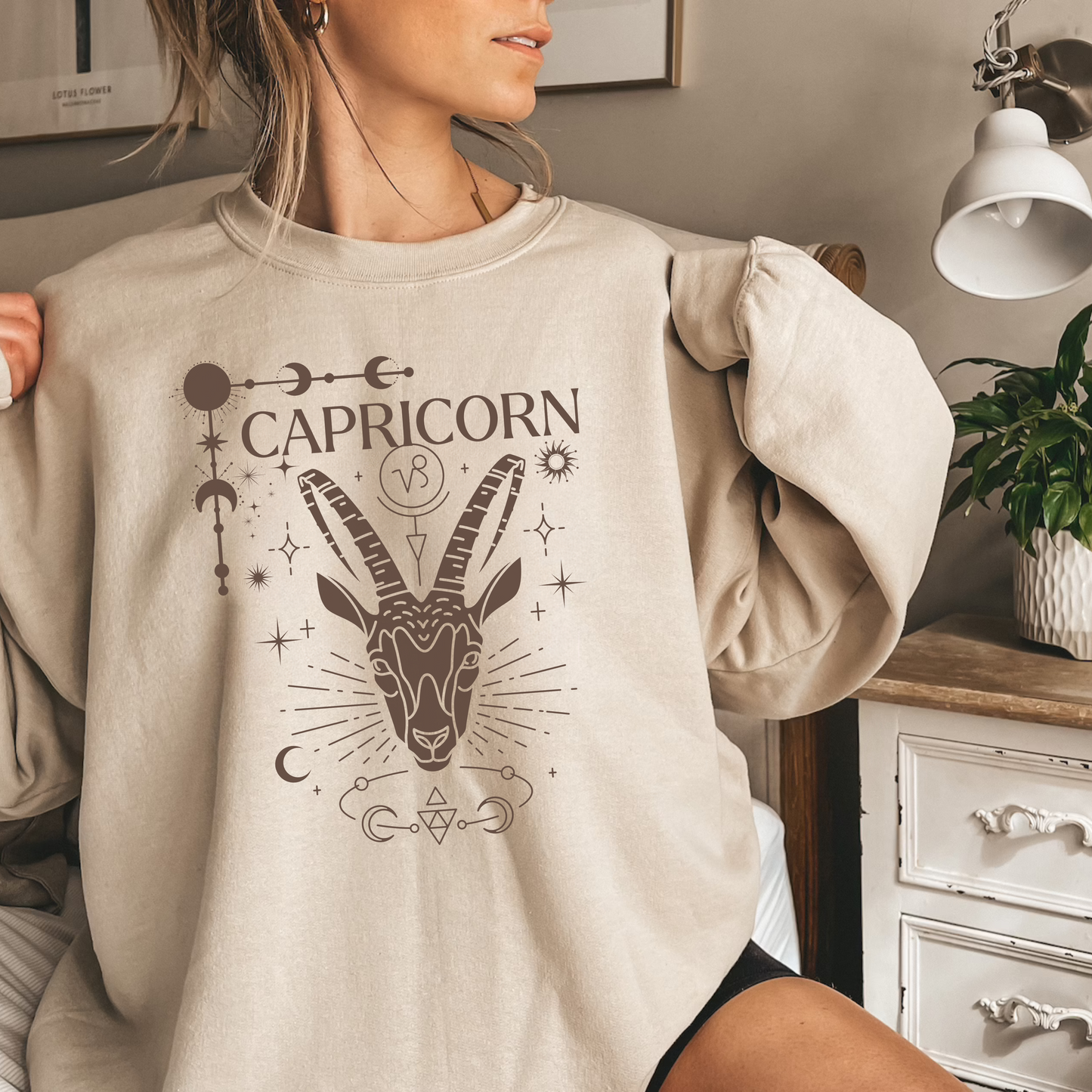 Front of sand Capricorn-themed sweatshirt featuring a glamorous illustration of a goat symbol with celestial and ornate details.