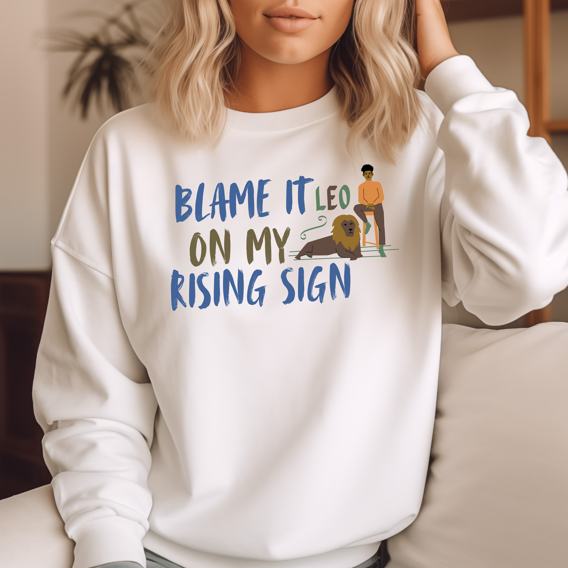 Front of white sweatshirt with Leo-themed design, text 'Blame It On My Rising Sign' featuring a person and a lion illustration.