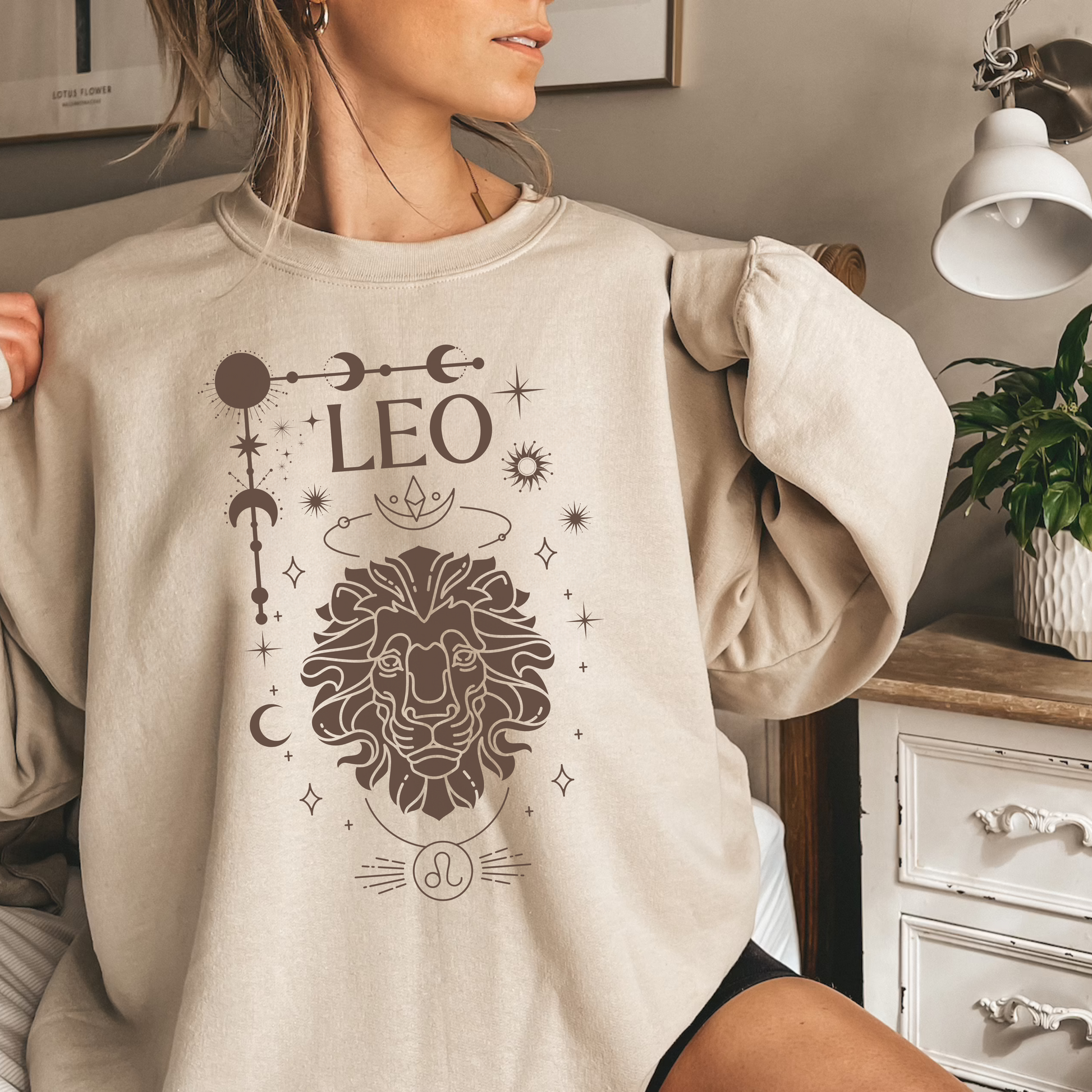 Front of sand sweatshirt featuring a Leo-themed glamour design with a stylized brown lion illustration and celestial symbols. Text reads 'Leo' with zodiac symbol.