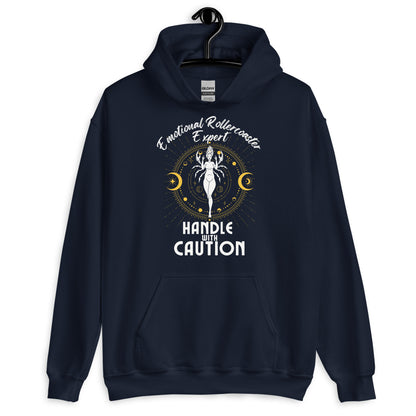 Navy blue hoodie featuring a Cancer zodiac-themed design with the phrase 'Emotional Rollercoaster Expert' at the top and 'Handle With Caution' at the bottom. The central illustration depicts a stylized figure surrounded by celestial symbols, including moons and stars, with a mystical, radiant backdrop in yellow accents.