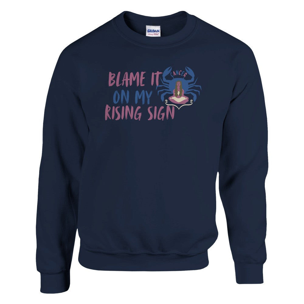 Navy blue sweatshirt with a Cancer zodiac-themed design featuring the phrase 'Blame It On My Rising Sign.' The design includes a colorful crab illustration with the word 'Cancer' above it and an abstract depiction of a person in a relaxed pose, conveying a playful astrology-inspired theme.