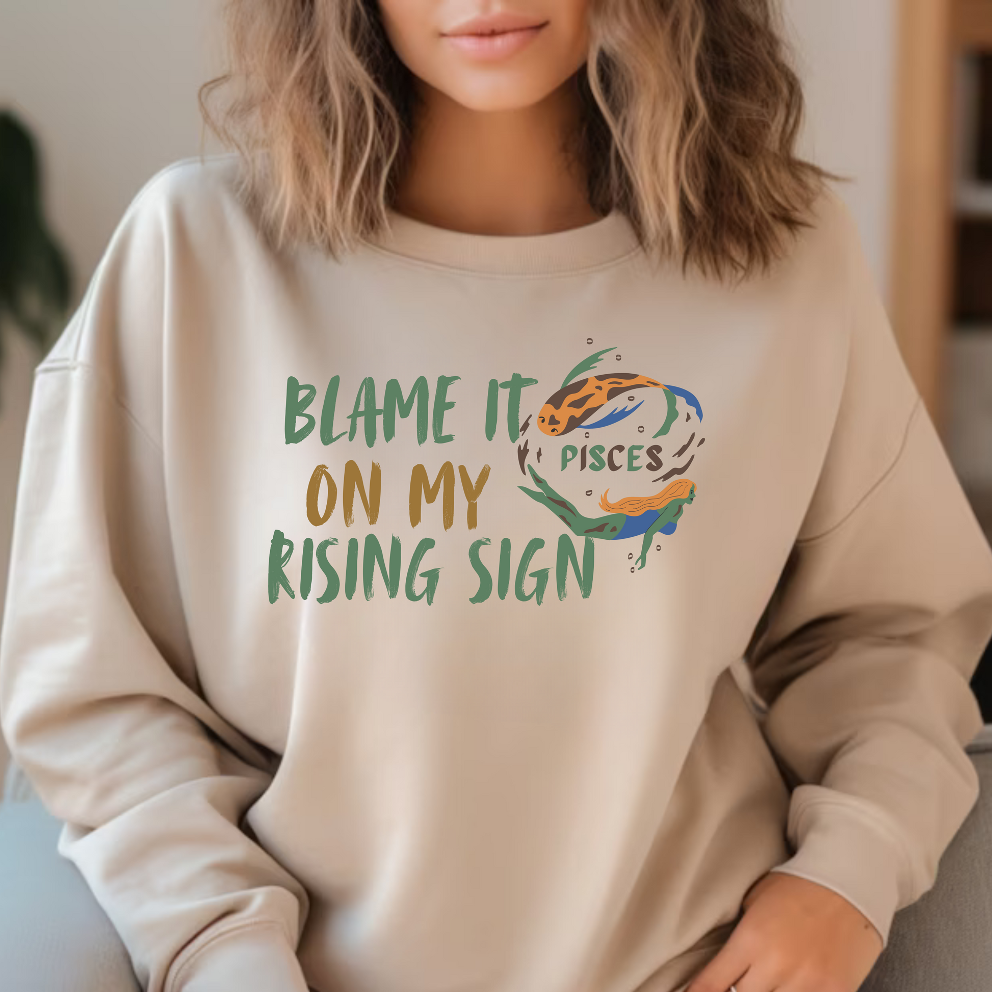 Sand Pisces sweatshirt with 'Blame it on my rising sign' text and colorful Pisces symbol illustration.