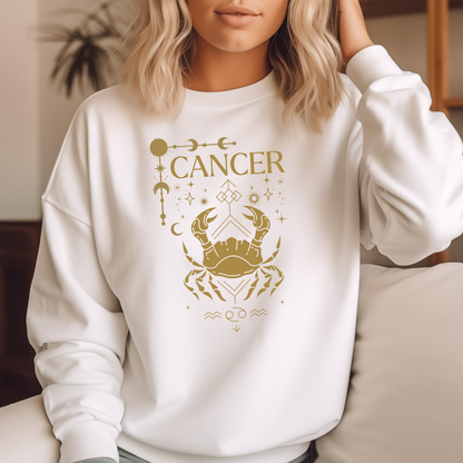 White sweatshirt featuring a Cancer zodiac design in a brownish-gold color. The central illustration shows a stylized crab with intricate celestial symbols, stars, and decorative accents surrounding it. The word 'Cancer' is displayed above, and the Cancer zodiac symbol appears below, giving the design a mystical and astrological aesthetic.