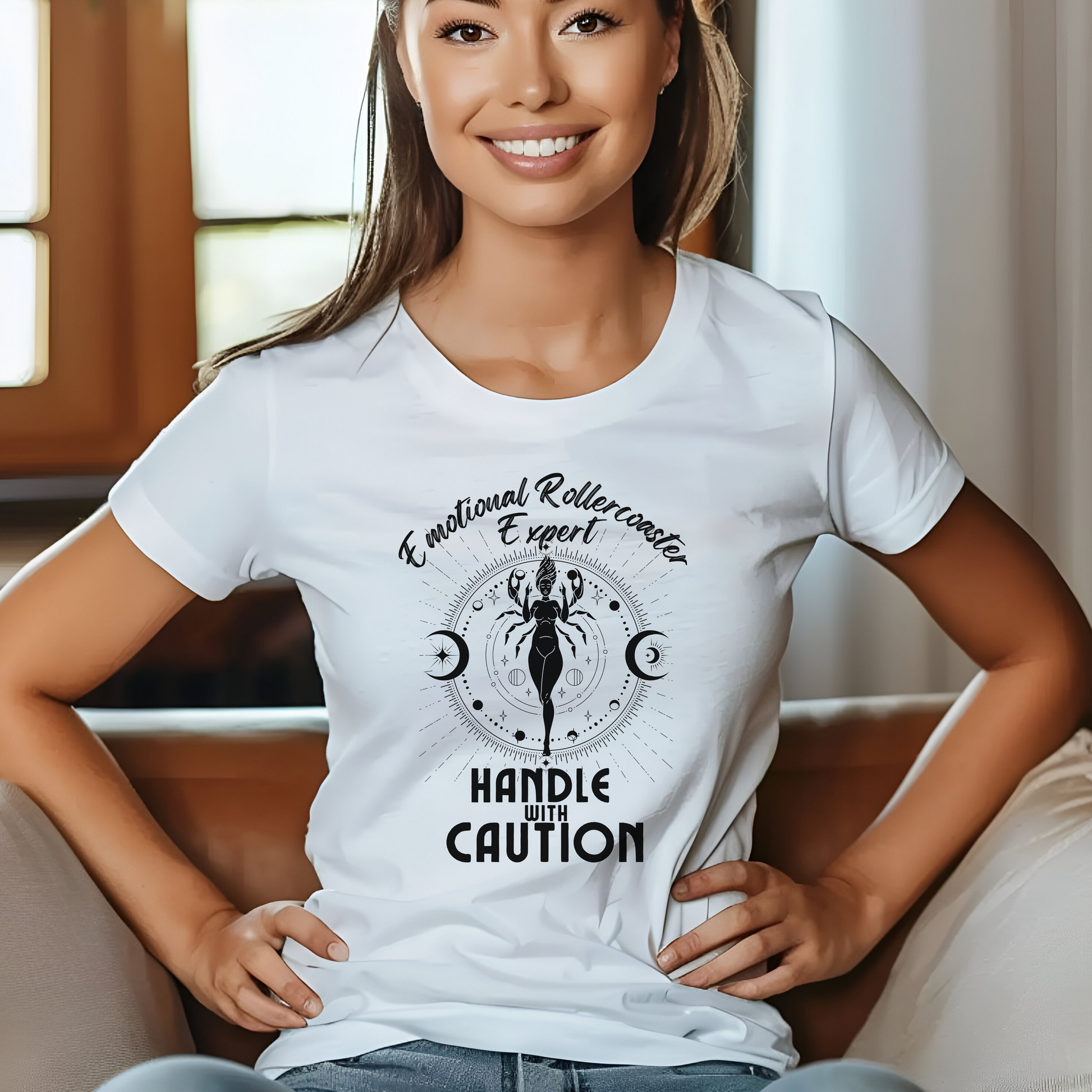 White t-shirt featuring a Cancer zodiac-themed design with the phrase 'Emotional Rollercoaster Expert' at the top and 'Handle With Caution' at the bottom. The central illustration displays a stylized figure in a mystical design surrounded by celestial symbols, including moons, against a radiant, detailed backdrop in black.